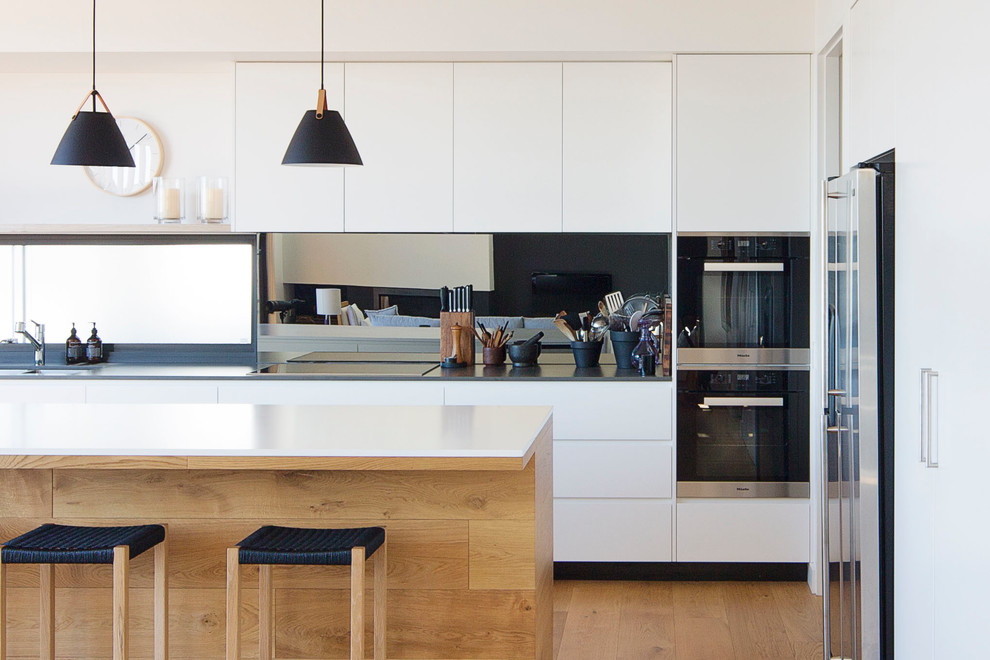 Design ideas for a large contemporary l-shaped open plan kitchen in Sydney with an undermount sink, flat-panel cabinets, white cabinets, quartz benchtops, metallic splashback, mirror splashback, stainless steel appliances, medium hardwood floors and with island.