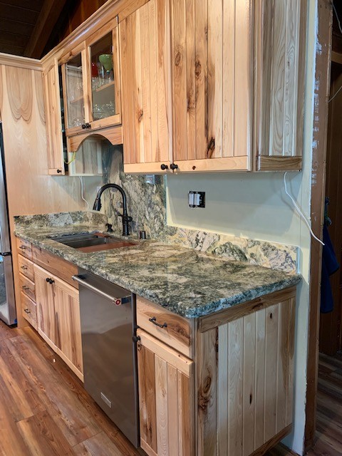Example of a mid-sized mountain style medium tone wood floor and brown floor open concept kitchen design with flat-panel cabinets, light wood cabinets, granite countertops, gray backsplash, stone slab backsplash, stainless steel appliances, gray countertops and an undermount sink