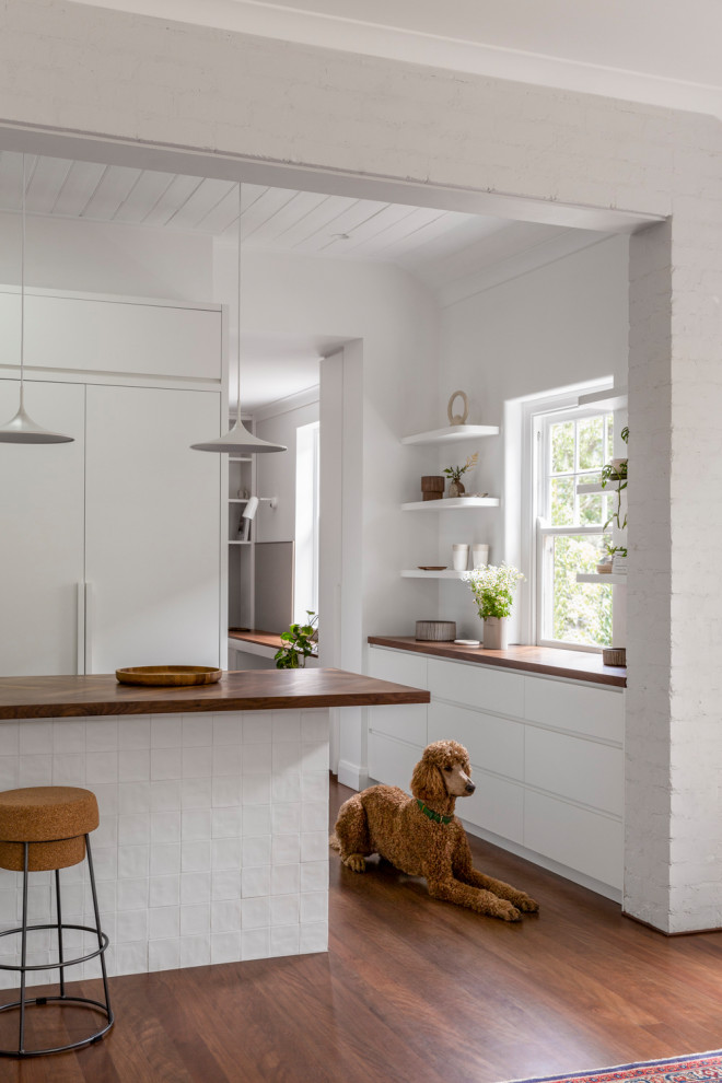 Inspiration för avskilda moderna brunt u-kök, med släta luckor, vita skåp, träbänkskiva, integrerade vitvaror, mellanmörkt trägolv, en köksö och brunt golv
