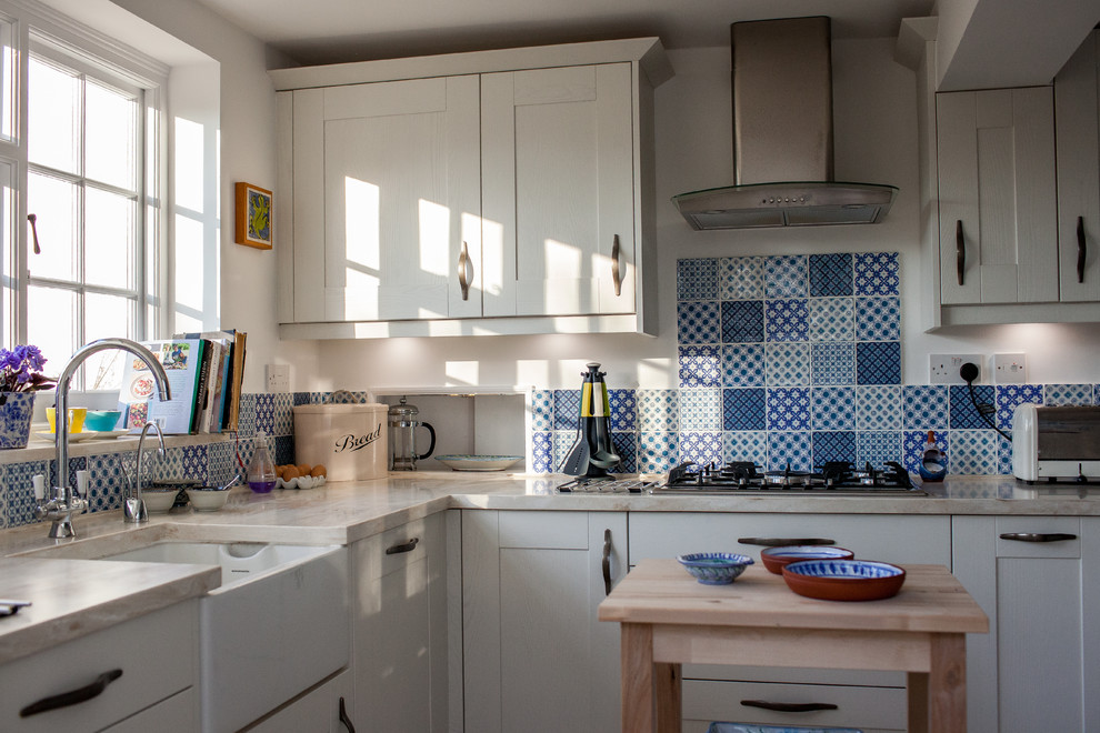 Inspiration for a mid-sized transitional l-shaped separate kitchen in Buckinghamshire with a farmhouse sink, shaker cabinets, beige cabinets, solid surface benchtops, blue splashback, ceramic splashback, stainless steel appliances, ceramic floors and no island.