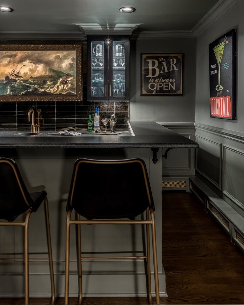 This is an example of a large transitional single-wall seated home bar in New York with an undermount sink, glass-front cabinets, black cabinets, soapstone benchtops, black splashback, glass tile splashback, dark hardwood floors, brown floor and black benchtop.