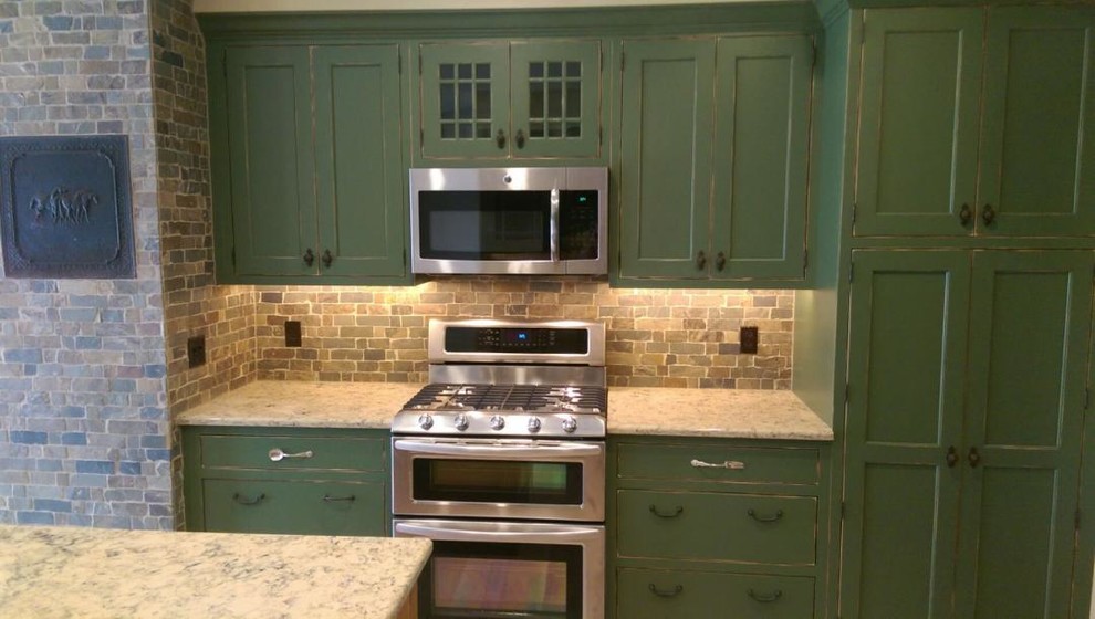 This is an example of a mid-sized country u-shaped kitchen in Other with shaker cabinets, green cabinets, granite benchtops, multi-coloured splashback, stone tile splashback, with island, a farmhouse sink, stainless steel appliances and light hardwood floors.