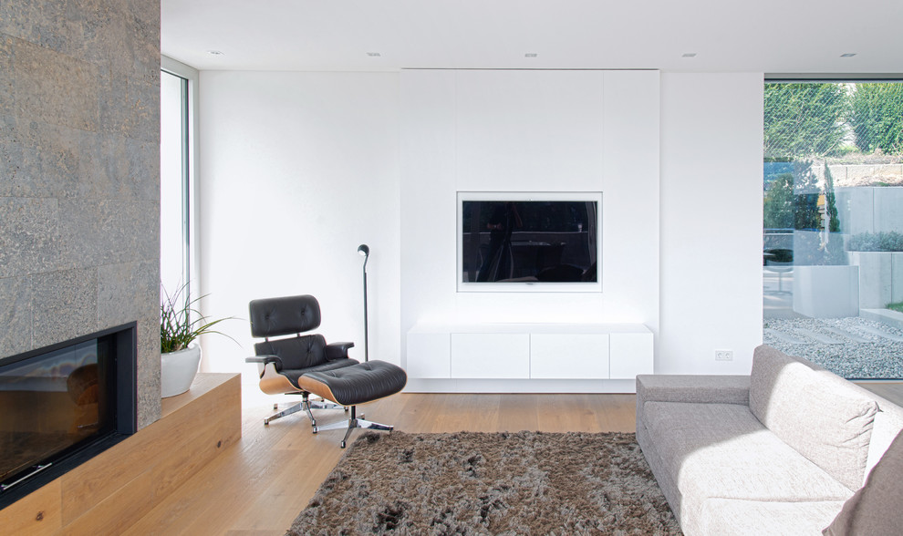 This is an example of a mid-sized modern open concept family room in Stuttgart with white walls, light hardwood floors, a ribbon fireplace and a wall-mounted tv.