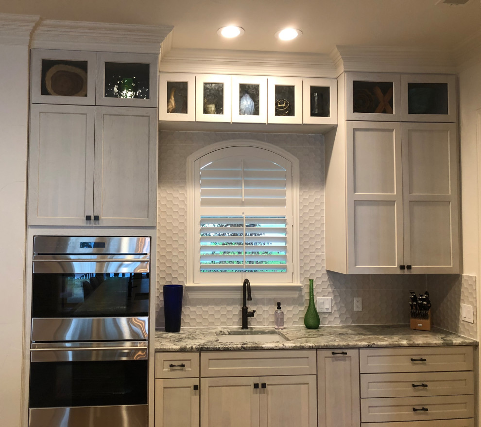 Bild på ett stort maritimt grå grått kök, med en undermonterad diskho, skåp i shakerstil, vita skåp, granitbänkskiva, grått stänkskydd, stänkskydd i porslinskakel, rostfria vitvaror, klinkergolv i porslin, en köksö och brunt golv