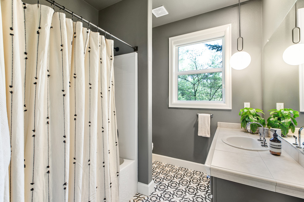 Mid-sized eclectic 3/4 ceramic tile, black floor and single-sink bathroom photo in Portland with raised-panel cabinets, black cabinets, a one-piece toilet, black walls, a drop-in sink, tile countertops, beige countertops and a built-in vanity