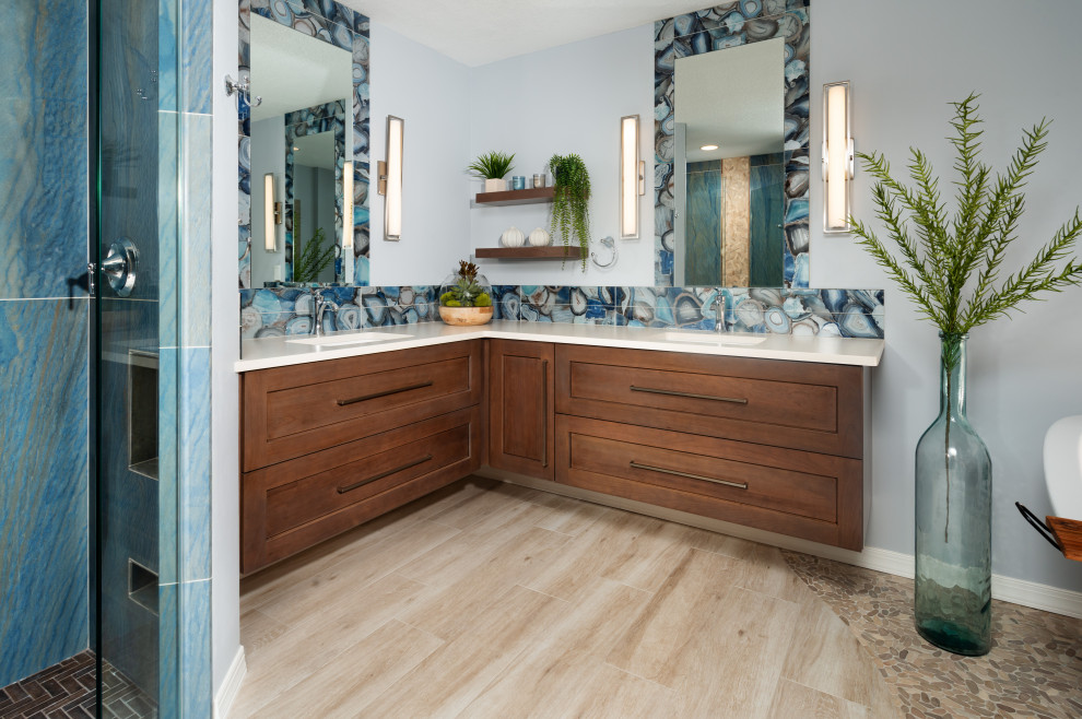 Photo of a mid-sized transitional master bathroom in Other with recessed-panel cabinets, medium wood cabinets, a freestanding tub, a curbless shower, a two-piece toilet, blue tile, glass tile, grey walls, porcelain floors, an undermount sink, quartzite benchtops, beige floor, a hinged shower door and beige benchtops.