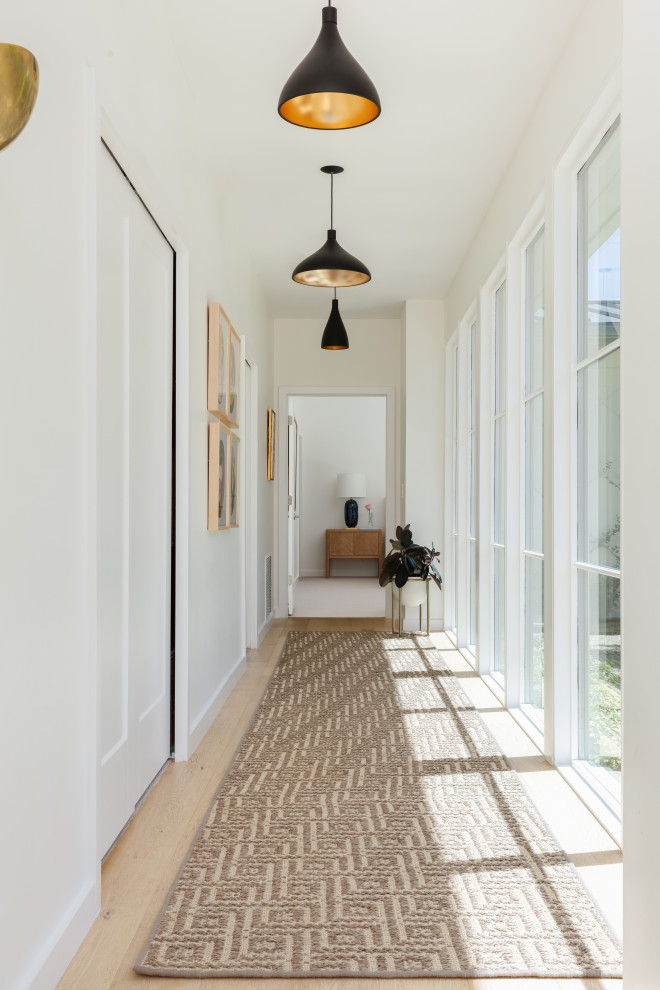 This is an example of a midcentury hallway in Austin with white walls and light hardwood floors.