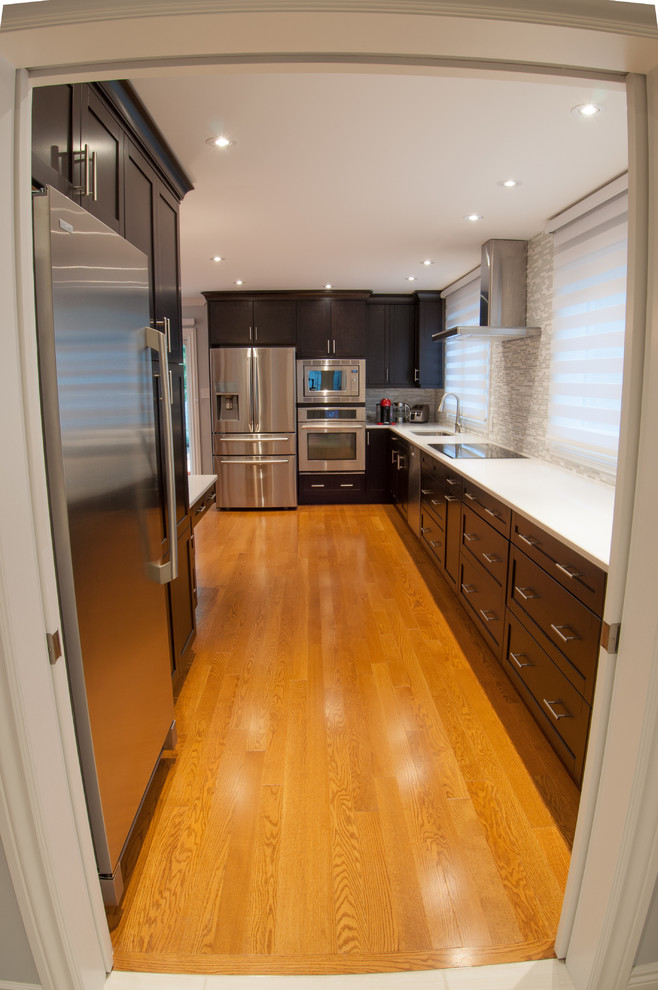 Large transitional galley light wood floor enclosed kitchen photo in Toronto with a single-bowl sink, shaker cabinets, dark wood cabinets, quartzite countertops, beige backsplash, stone tile backsplash, stainless steel appliances and an island