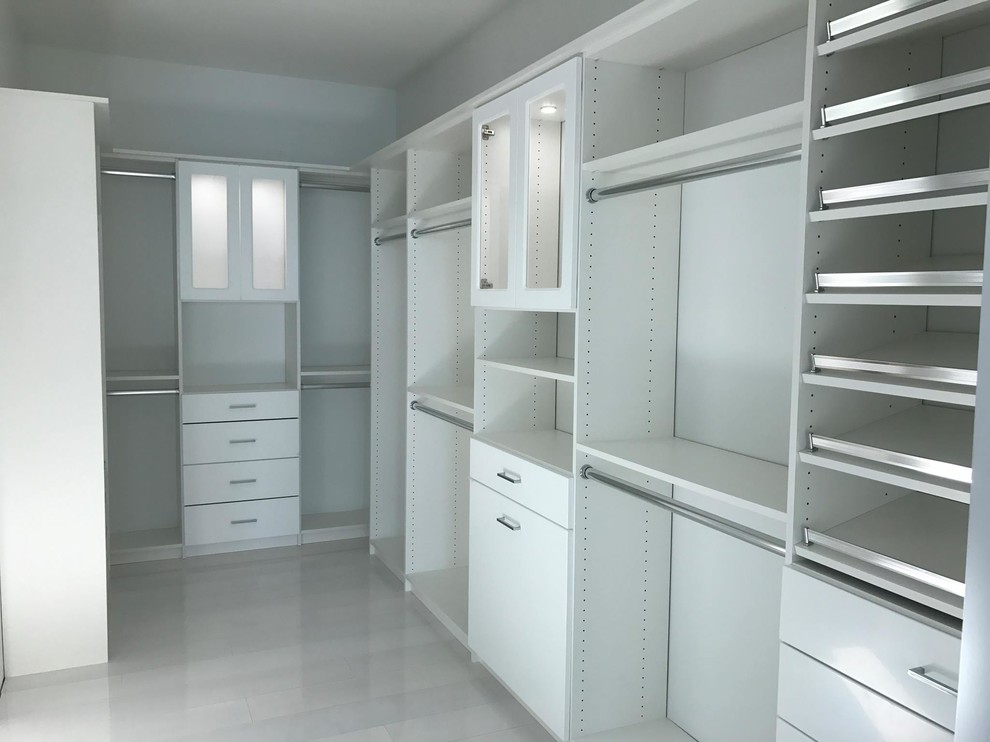 This is an example of a large traditional gender-neutral walk-in wardrobe in Other with glass-front cabinets, white cabinets, travertine floors and beige floor.