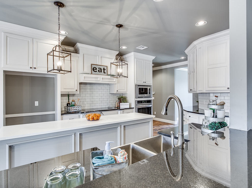 This is an example of a large country galley open plan kitchen in Oklahoma City with a farmhouse sink, raised-panel cabinets, white cabinets, granite benchtops, white splashback, subway tile splashback, stainless steel appliances, medium hardwood floors and with island.
