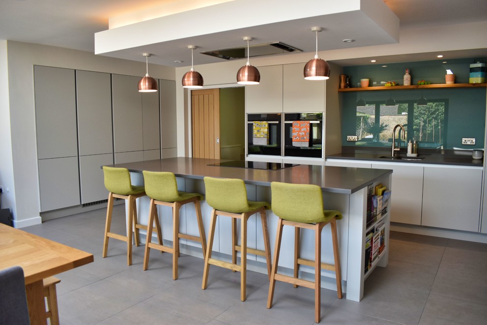 This is an example of a large contemporary u-shaped eat-in kitchen in Cambridgeshire with flat-panel cabinets, beige cabinets, with island, an undermount sink, green splashback, stainless steel appliances, grey floor and black benchtop.