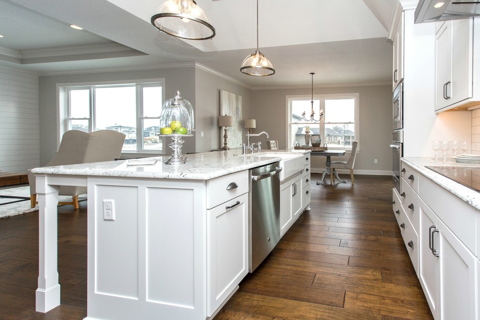 Mid-sized transitional single-wall medium tone wood floor and beige floor open concept kitchen photo with a farmhouse sink, recessed-panel cabinets, white cabinets, granite countertops, white backsplash, ceramic backsplash, stainless steel appliances and an island