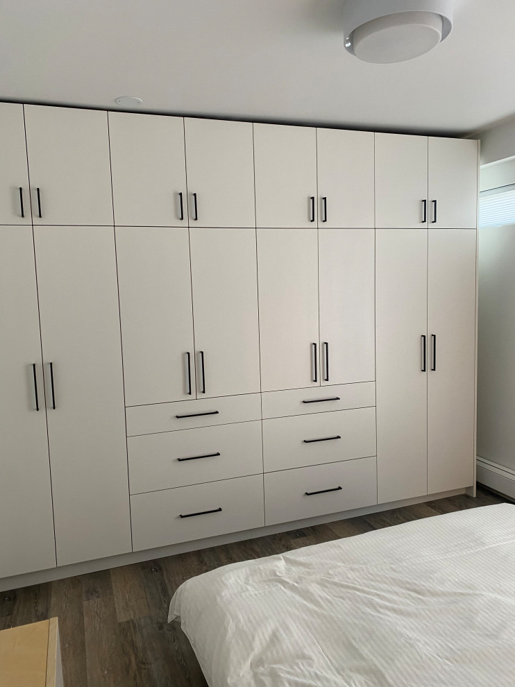 Photo of a gender-neutral storage and wardrobe in Vancouver with flat-panel cabinets, white cabinets, vinyl floors and brown floor.