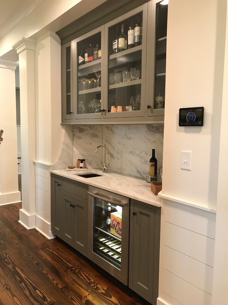 Design ideas for a large arts and crafts single-wall wet bar in Other with a drop-in sink, recessed-panel cabinets, grey cabinets, granite benchtops, white splashback, marble splashback, medium hardwood floors, brown floor and white benchtop.