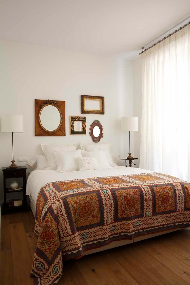 Inspiration for a mid-sized traditional bedroom in Madrid with white walls, medium hardwood floors and brown floor.