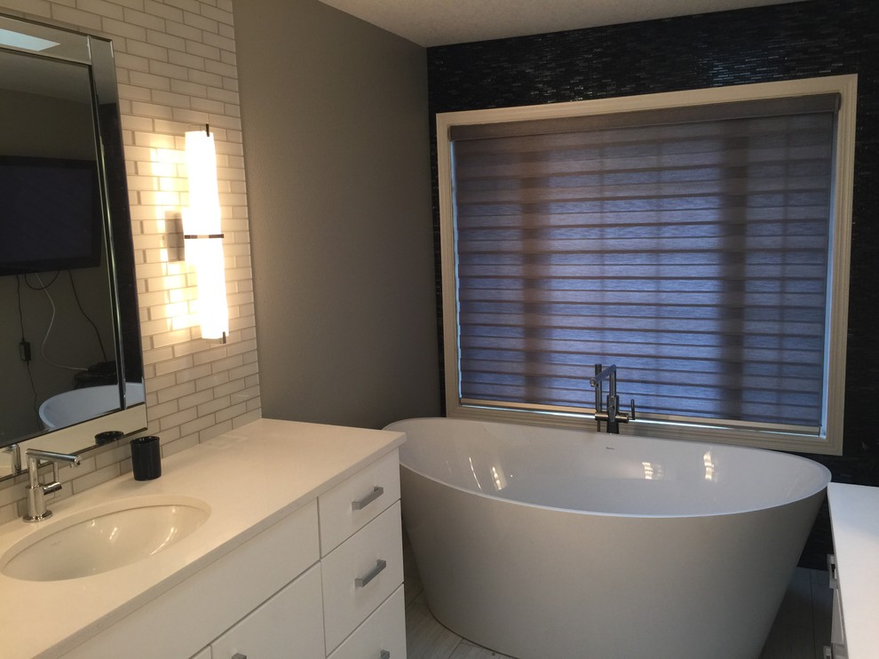 Example of a mid-sized transitional master white tile and subway tile porcelain tile and gray floor freestanding bathtub design with flat-panel cabinets, gray walls, an undermount sink, quartzite countertops and white cabinets