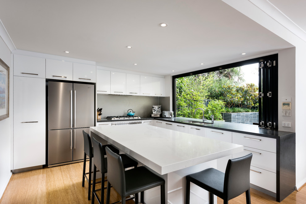 Photo of a mid-sized contemporary l-shaped eat-in kitchen in Perth with a double-bowl sink, recessed-panel cabinets, white cabinets, quartz benchtops, metallic splashback, ceramic splashback, stainless steel appliances, medium hardwood floors and with island.