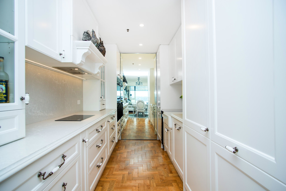 Design ideas for a mid-sized traditional galley eat-in kitchen in Sydney with a farmhouse sink, recessed-panel cabinets, white cabinets, quartz benchtops, white splashback, stone slab splashback, panelled appliances, light hardwood floors, no island and brown floor.
