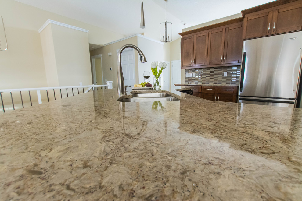 Example of a mid-sized transitional l-shaped ceramic tile and beige floor eat-in kitchen design in Edmonton with a double-bowl sink, shaker cabinets, brown cabinets, quartz countertops, beige backsplash, glass tile backsplash, stainless steel appliances and an island