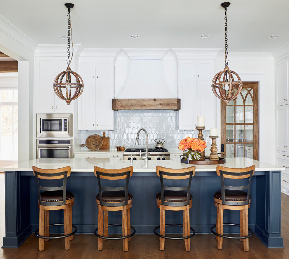 Design ideas for a beach style kitchen in Raleigh with shaker cabinets, white cabinets, white splashback, stainless steel appliances, dark hardwood floors, with island and white benchtop.
