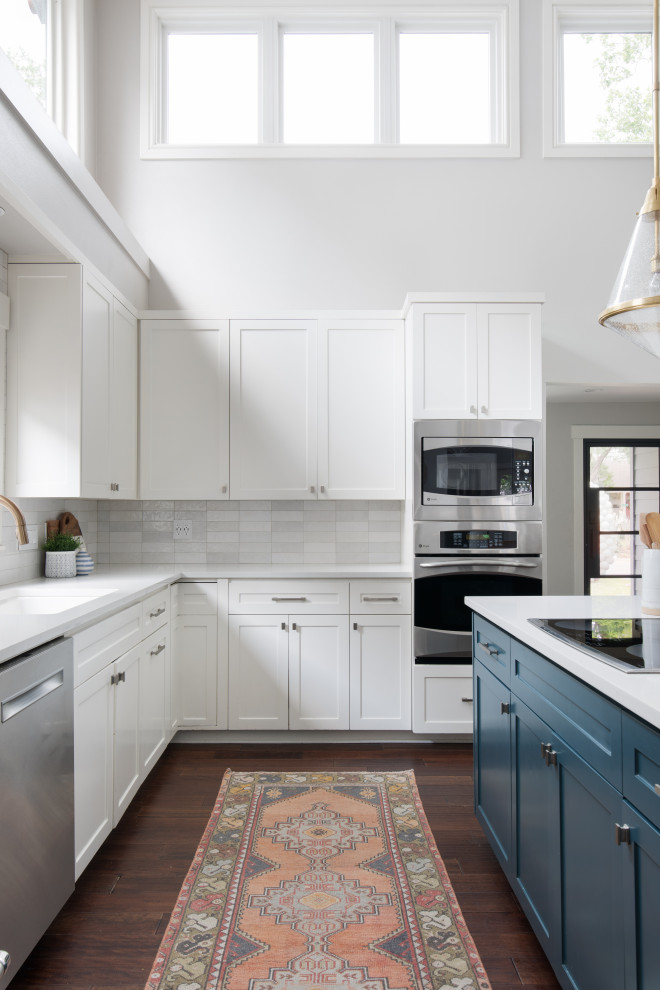Example of a large transitional l-shaped dark wood floor, brown floor and vaulted ceiling open concept kitchen design in Austin with an undermount sink, shaker cabinets, white cabinets, quartz countertops, gray backsplash, subway tile backsplash, stainless steel appliances, an island and white countertops