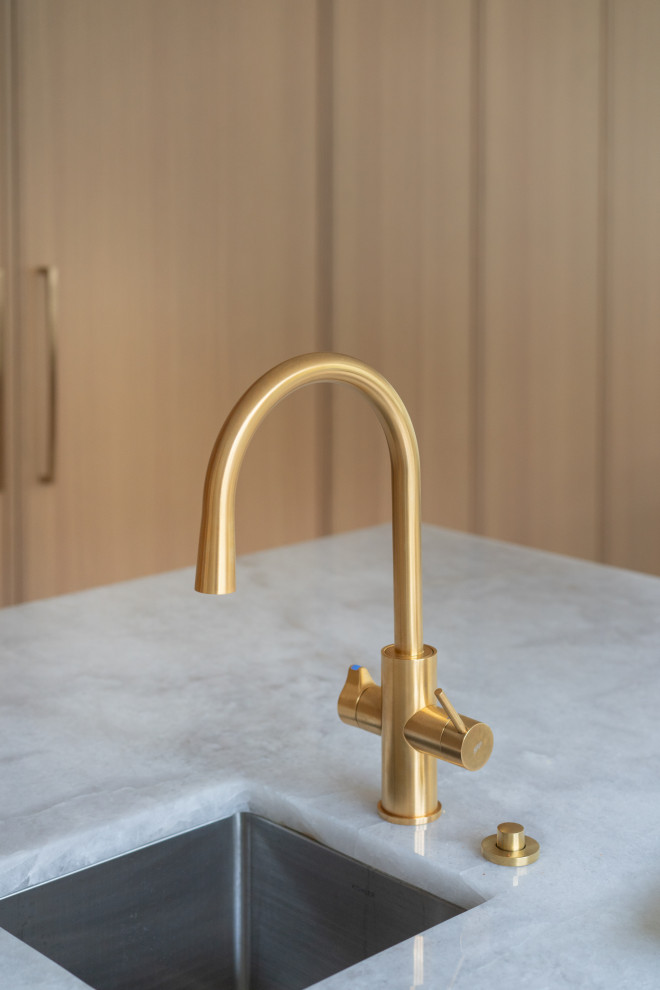 An elegant and modern kitchen faucet with a gold finish, placed near a large win