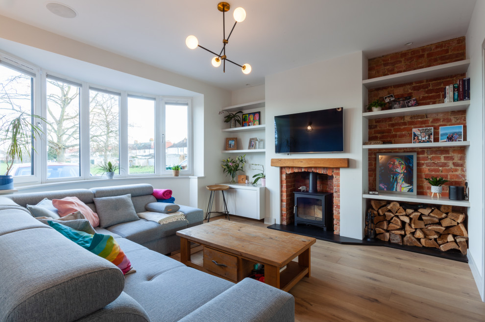 Medium sized contemporary open plan living room in London with light hardwood flooring, a wood burning stove and a brick fireplace surround.