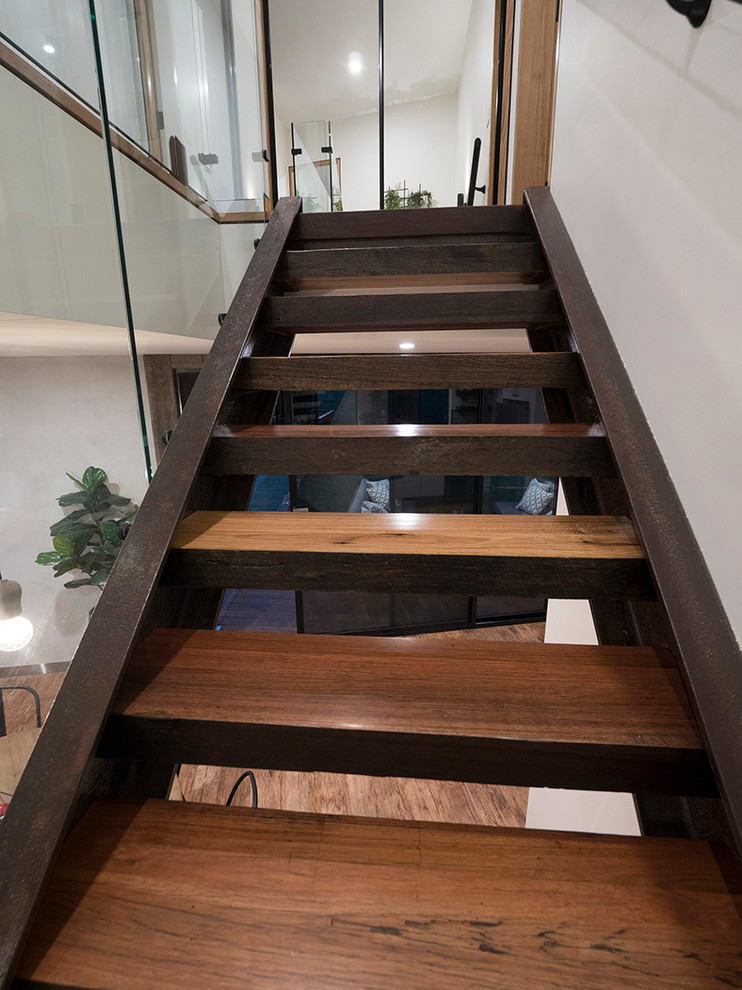 Design ideas for an industrial wood staircase in Other with metal risers and glass railing.
