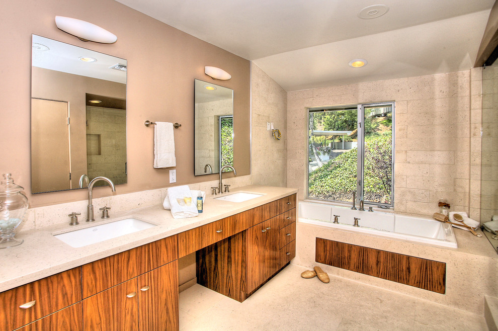 Midcentury bathroom in Los Angeles with an undermount sink, flat-panel cabinets, medium wood cabinets, limestone benchtops, a drop-in tub, an alcove shower, beige tile and stone tile.