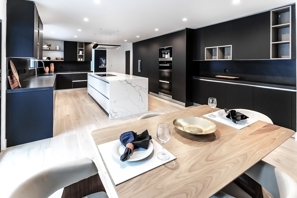 Inspiration for a mid-sized modern l-shaped eat-in kitchen in Los Angeles with a double-bowl sink, black cabinets, marble benchtops, black splashback, porcelain splashback, black appliances, painted wood floors, with island, beige floor and black benchtop.