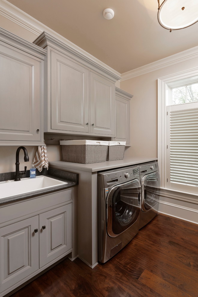 Inspiration for an expansive traditional galley utility room in DC Metro with a drop-in sink, beaded inset cabinets, grey cabinets, granite benchtops, beige walls, dark hardwood floors, a side-by-side washer and dryer and brown floor.