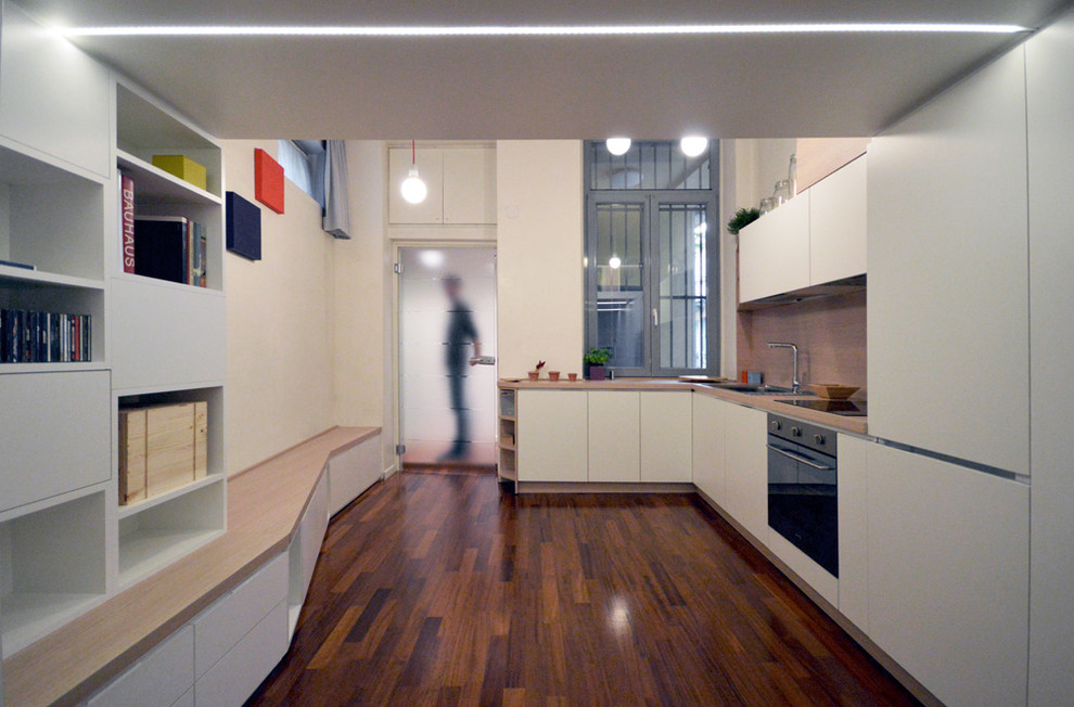 Photo of a small contemporary l-shaped open plan kitchen in Milan with flat-panel cabinets, white cabinets, laminate benchtops, brown splashback, timber splashback, stainless steel appliances and brown benchtop.