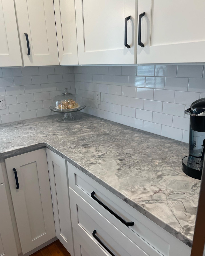 This is an example of a small modern l-shaped separate kitchen in Boston with a single-bowl sink, shaker cabinets, white cabinets, quartzite benchtops, white splashback, subway tile splashback, stainless steel appliances, medium hardwood floors, no island, brown floor and white benchtop.