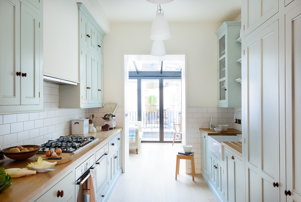 Mid-sized traditional galley separate kitchen in London with a double-bowl sink, beaded inset cabinets, blue cabinets, wood benchtops, white splashback, subway tile splashback, stainless steel appliances, light hardwood floors and no island.