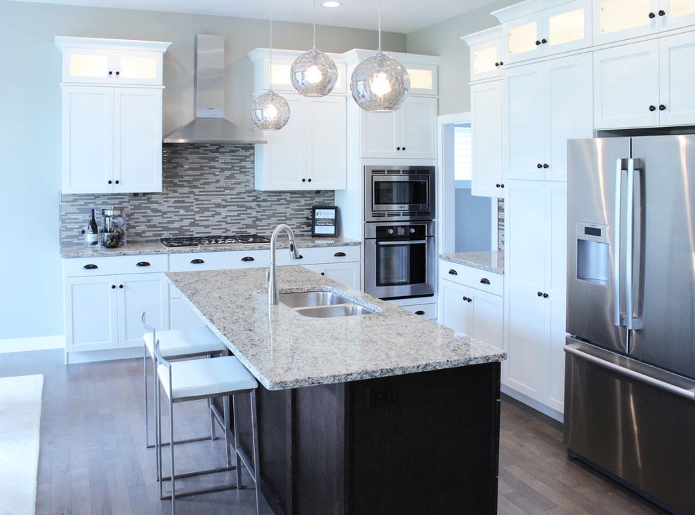Mid-sized transitional l-shaped medium tone wood floor eat-in kitchen photo in Cedar Rapids with an undermount sink, shaker cabinets, white cabinets, granite countertops, gray backsplash, matchstick tile backsplash, stainless steel appliances and an island