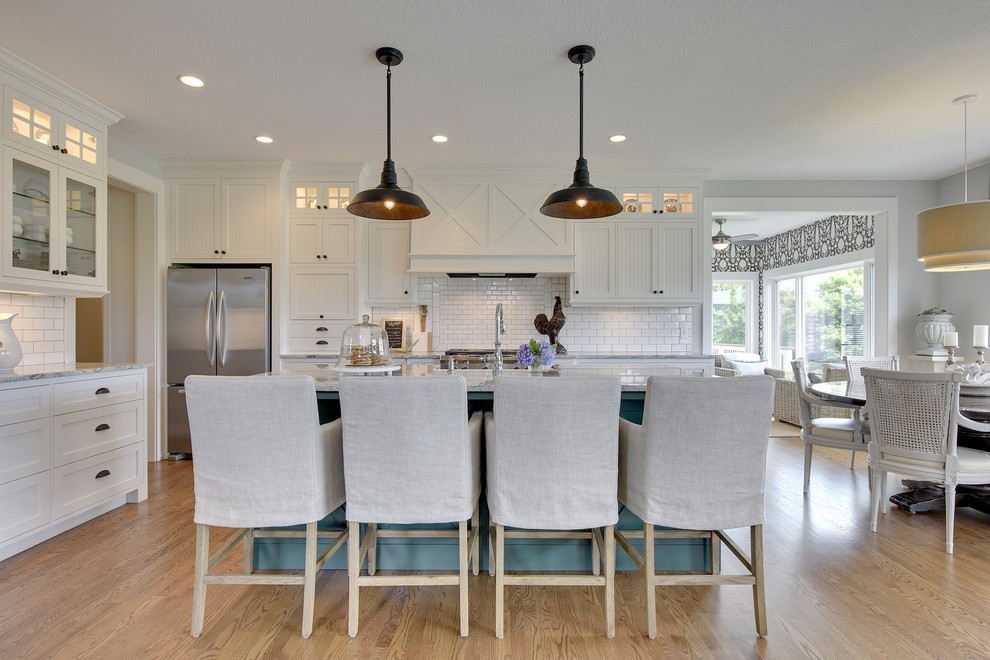 Inspiration for a country l-shaped eat-in kitchen in Minneapolis with white cabinets, granite benchtops, white splashback, ceramic splashback, stainless steel appliances, with island, shaker cabinets and medium hardwood floors.