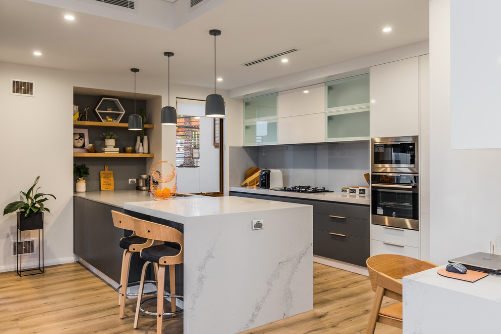 This is an example of a contemporary eat-in kitchen in Perth with flat-panel cabinets, grey cabinets, grey splashback, glass sheet splashback, stainless steel appliances, light hardwood floors, a peninsula, beige floor and grey benchtop.