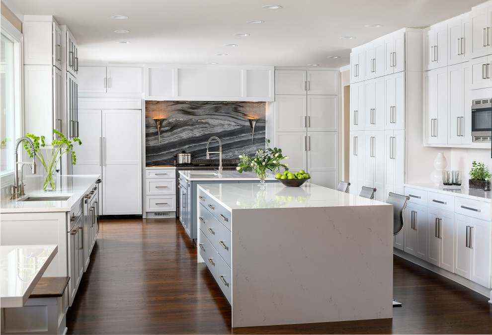 Inspiration for an expansive contemporary u-shaped kitchen pantry in Atlanta with a submerged sink, shaker cabinets, white cabinets, engineered stone countertops, grey splashback, marble splashback, stainless steel appliances, medium hardwood flooring, multiple islands, brown floors, white worktops and a feature wall.