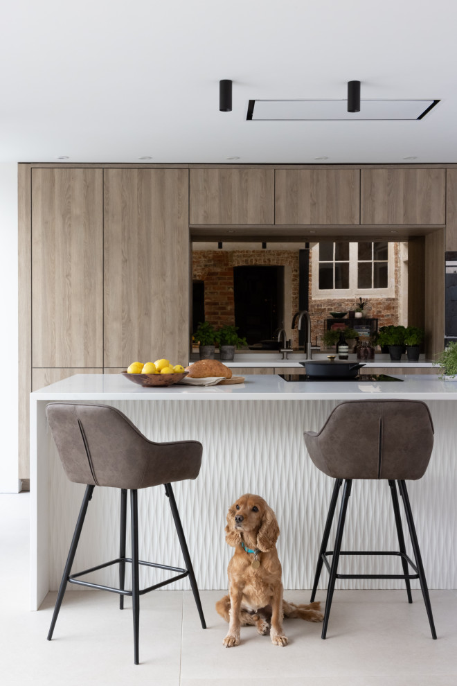 This is an example of a medium sized scandi kitchen/diner in Hampshire with flat-panel cabinets, medium wood cabinets, composite countertops, mirror splashback, black appliances, an island and white worktops.