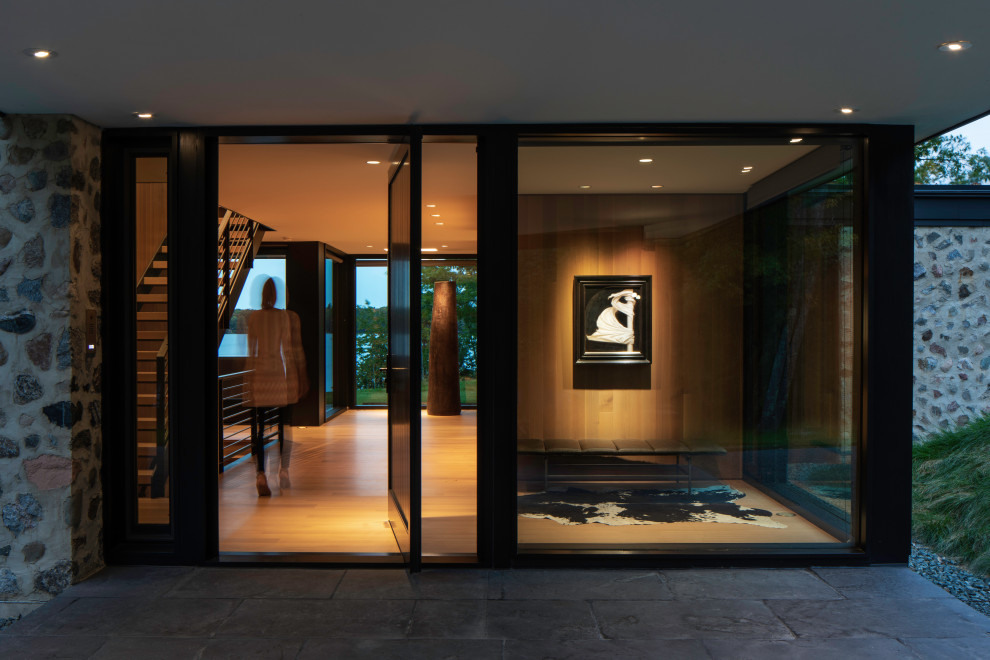 Photo of a large contemporary foyer in Other with brown walls, light hardwood floors, a pivot front door, a black front door, brown floor and wood walls.