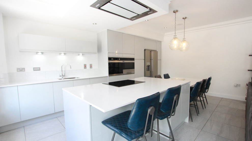 Photo of a large contemporary galley open plan kitchen in Glasgow with an integrated sink, flat-panel cabinets, grey cabinets, quartzite benchtops, white splashback, granite splashback, black appliances, porcelain floors, with island, grey floor, white benchtop and recessed.