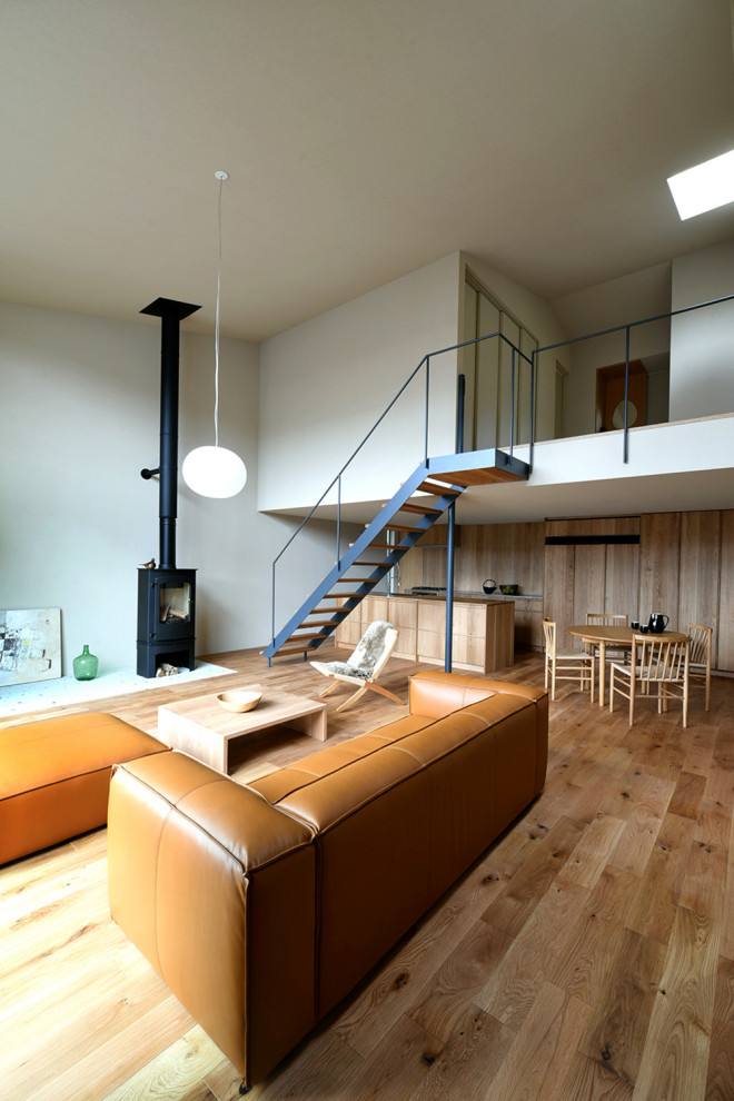 Esempio di un grande soggiorno minimalista aperto con pareti grigie, parquet chiaro, stufa a legna, cornice del camino in pietra e TV autoportante