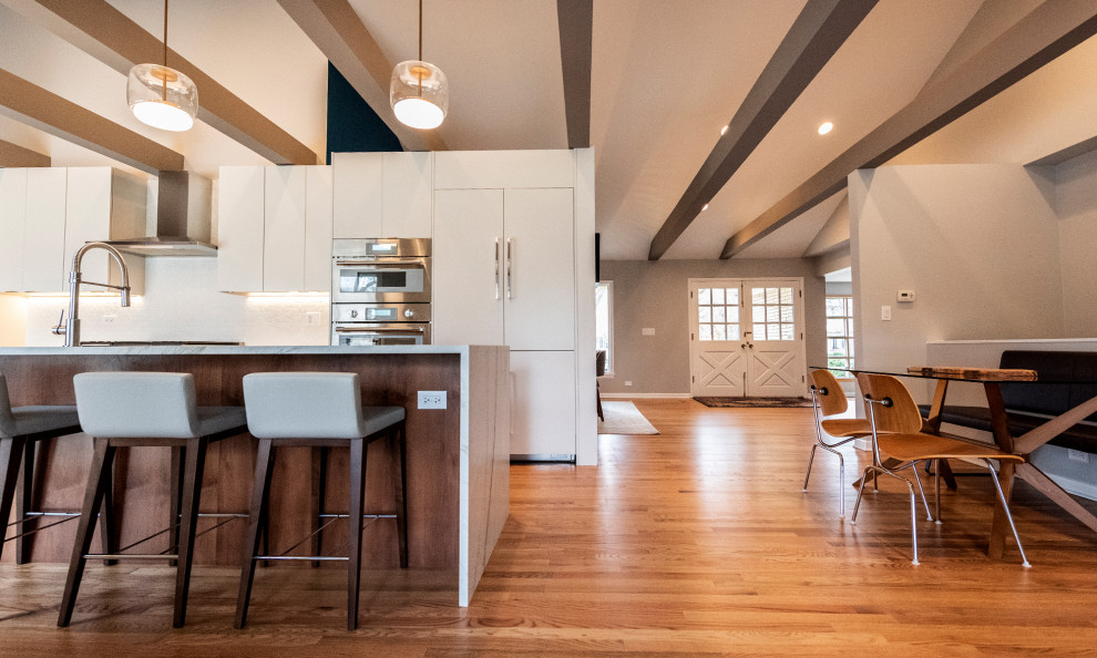 Photo of a large midcentury galley open plan kitchen in Chicago with an undermount sink, flat-panel cabinets, medium wood cabinets, quartzite benchtops, white splashback, mosaic tile splashback, panelled appliances, medium hardwood floors, with island, brown floor and white benchtop.