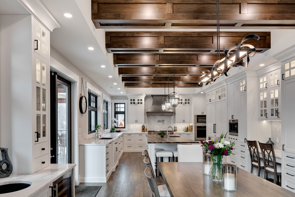 Inspiration for a huge transitional u-shaped dark wood floor and brown floor kitchen remodel in Calgary with an undermount sink, shaker cabinets, white cabinets, marble countertops, white backsplash, marble backsplash, stainless steel appliances, an island and white countertops