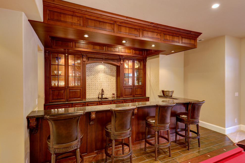 Photo of a mid-sized traditional single-wall seated home bar in Denver with glass-front cabinets, red cabinets, granite benchtops and beige splashback.