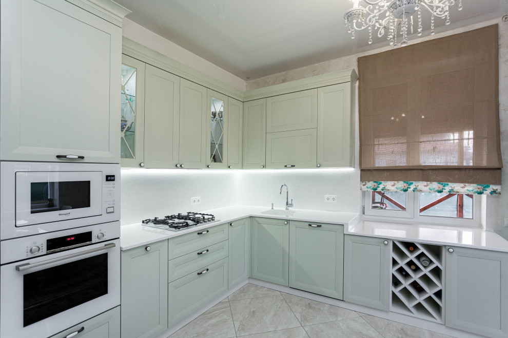 This is an example of a mid-sized transitional l-shaped eat-in kitchen in Other with an integrated sink, raised-panel cabinets, solid surface benchtops, white splashback, engineered quartz splashback, white appliances, ceramic floors, beige floor and white benchtop.