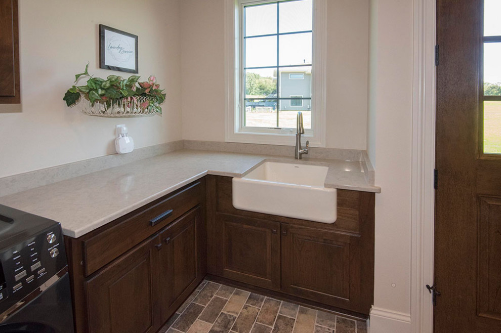 Large transitional utility room in Milwaukee with a farmhouse sink, raised-panel cabinets, medium wood cabinets, quartz benchtops, beige walls, brick floors, a side-by-side washer and dryer, beige floor and beige benchtop.