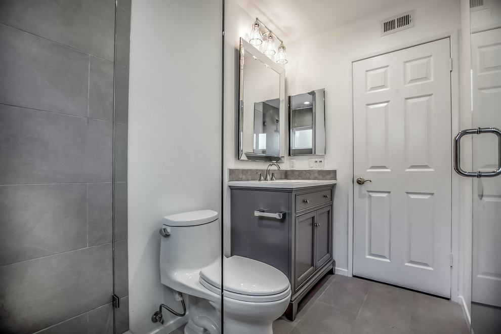 Photo of a small mediterranean 3/4 bathroom in Los Angeles with shaker cabinets, grey cabinets, an alcove shower, a one-piece toilet, gray tile, porcelain tile, grey walls, porcelain floors, a console sink, solid surface benchtops, grey floor and a hinged shower door.