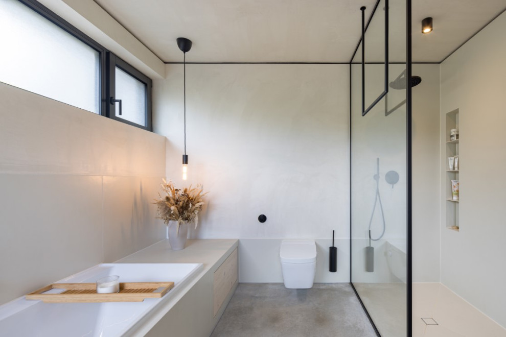 This is an example of a modern bathroom in Frankfurt with a drop-in tub, a wall-mount toilet, grey walls, concrete floors, an open shower, a double vanity and a floating vanity.