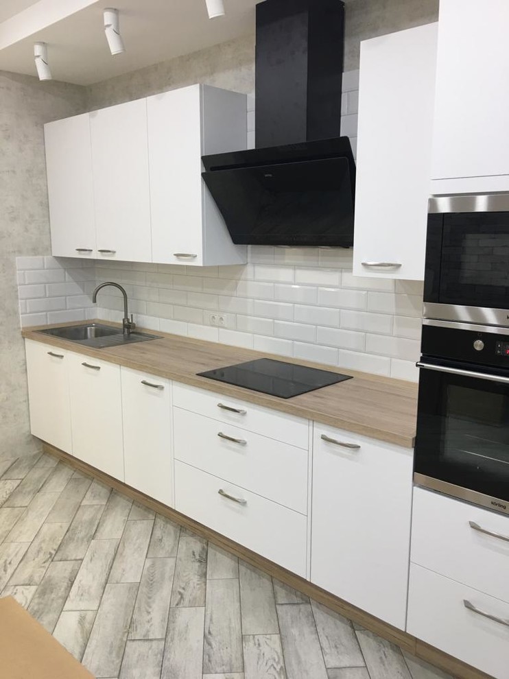 Photo of a mid-sized scandinavian single-wall kitchen pantry in Other with a drop-in sink, flat-panel cabinets, white cabinets, laminate benchtops, white splashback, subway tile splashback, black appliances, porcelain floors, no island, grey floor and beige benchtop.